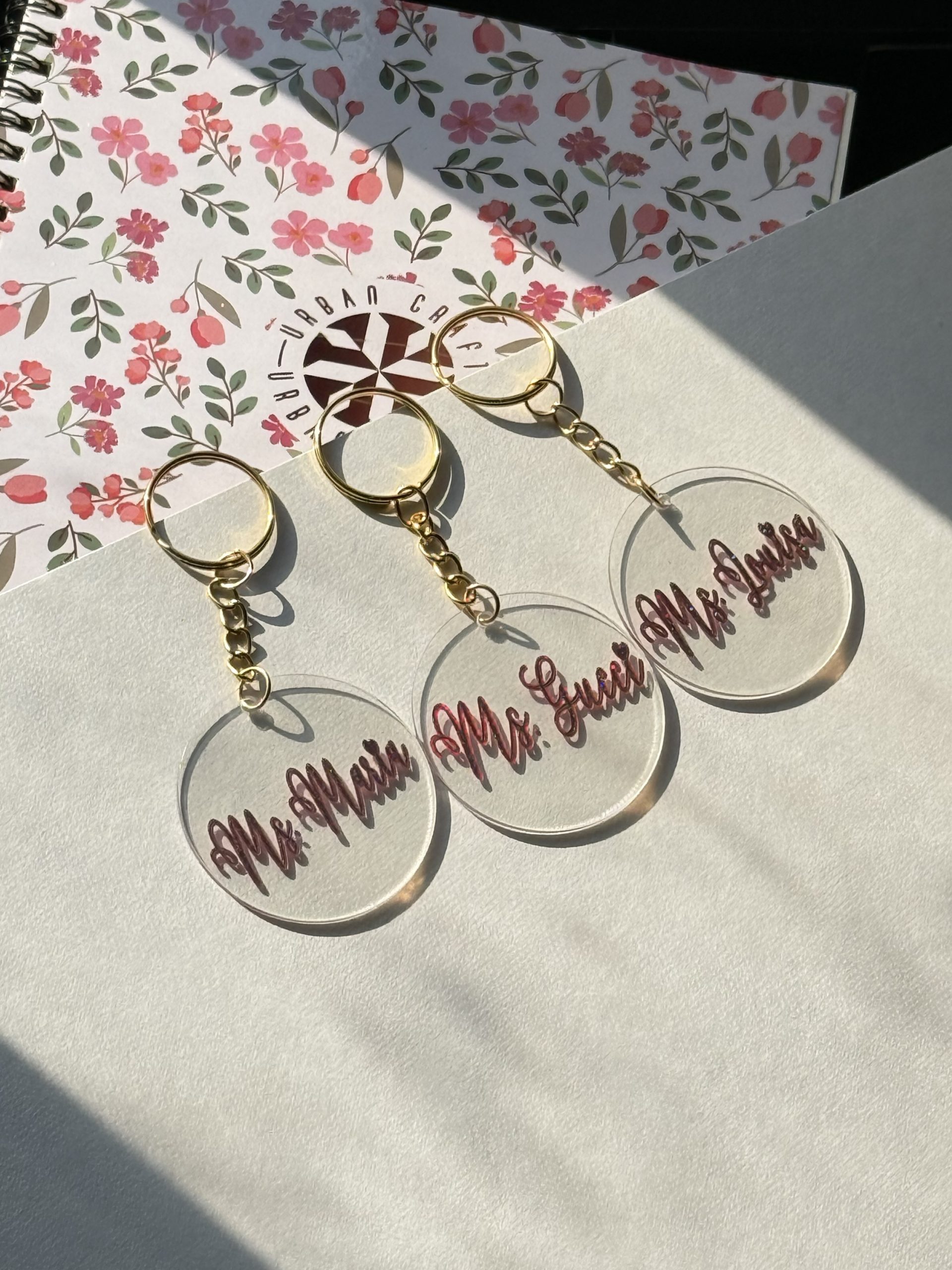 Round acrylic name keychains displayed with gold-colored rings