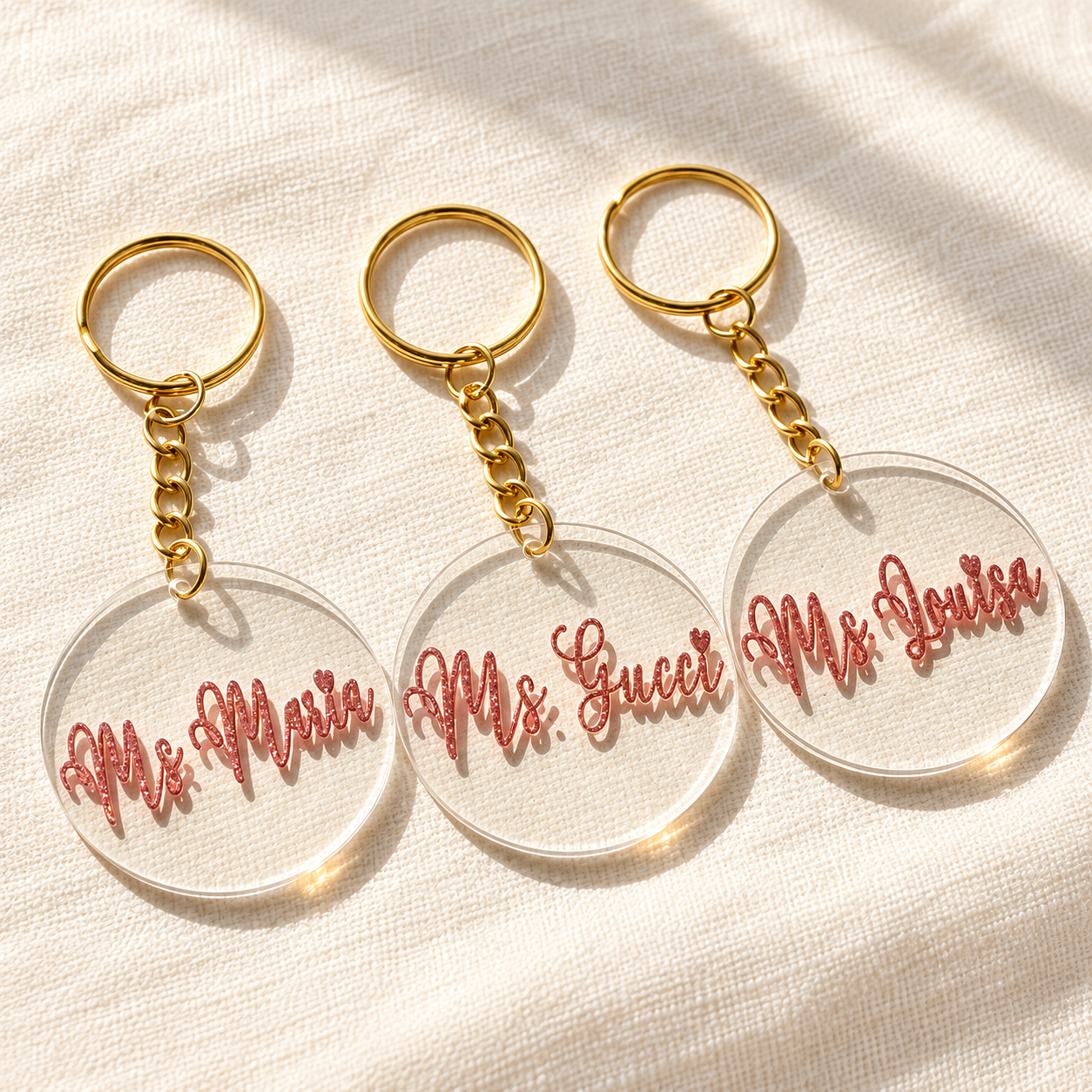 Actual transparent round acrylic name keychains with pink glitter lettering and gold rings, photographed in soft light